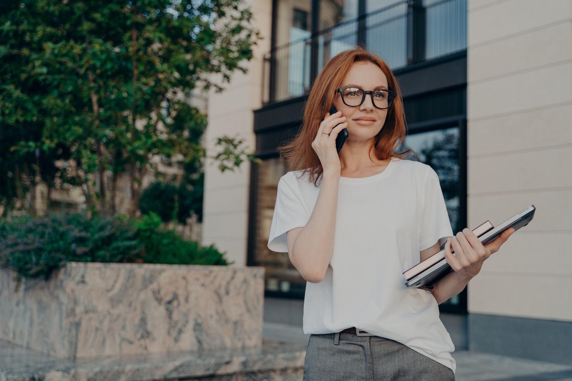 Thoughtful redhead woman looks into distance makes phone call holds smartphone near ear-letsworkabroad